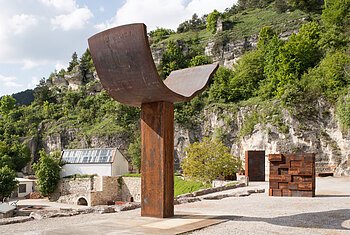 Alf Lechner - Skulpturenpark und Wohnhaus, Obereichstätt Große Metallskulptur in einer Landschaft mit Felsen und Bäumen im Hintergrund.