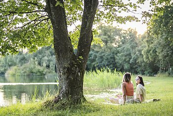 Pause am Leitnerweiher Zwei Frauen liegen auf einer Decke am Leitnerweiher, auch Weicheringer See genannt, und unterhalten sich.