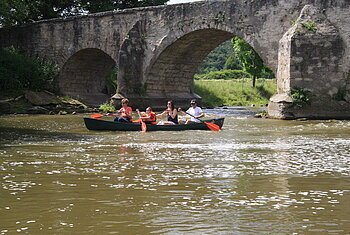 Bootsfahrer an der Steinbrücke bei Pfünz. Eine Familie ist einem Kanu vom Schmidt Bootsverleih auf der Altmühl unterwegs. Sie sind gerade unter der Steinbrücke hindurchgefahren, diese ist in Teilen noch zu sehen.